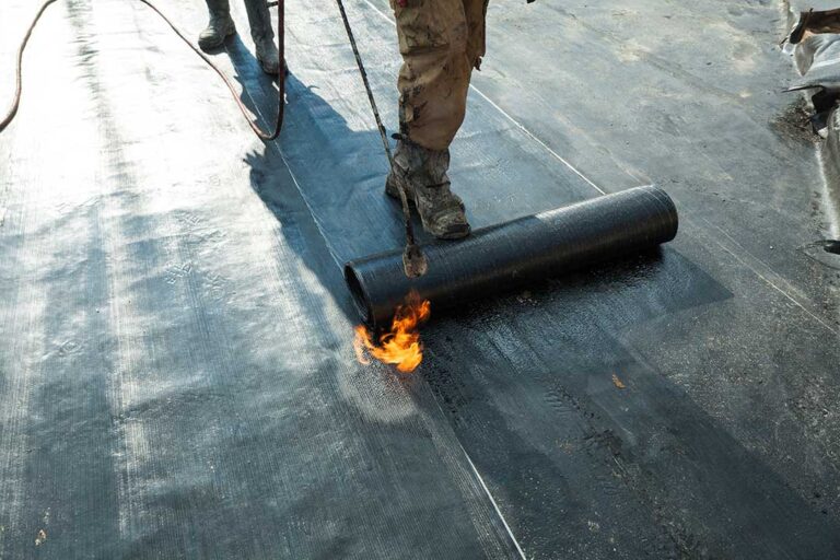 Two residential roof sections show gray metal panels beside layered asphalt shingles after a light snowfall.